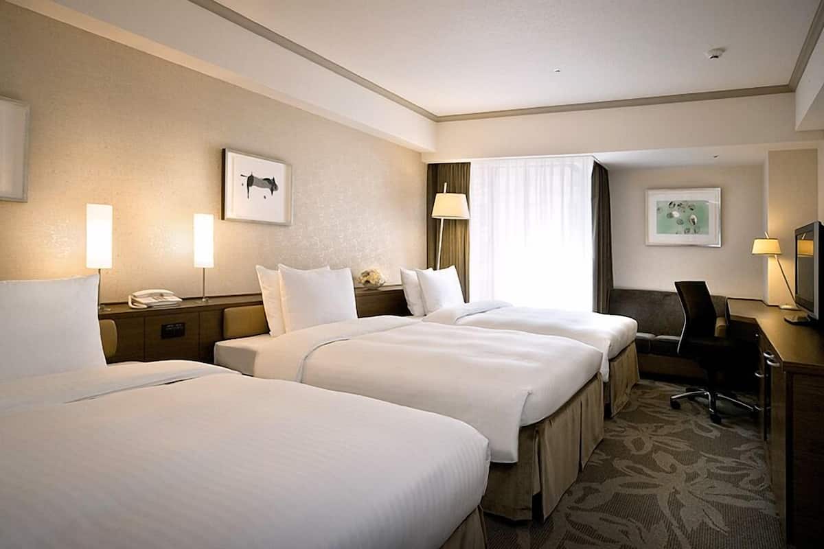 Une chambre d’hôtel avec trois lits, un bureau, une chaise et une télévision.