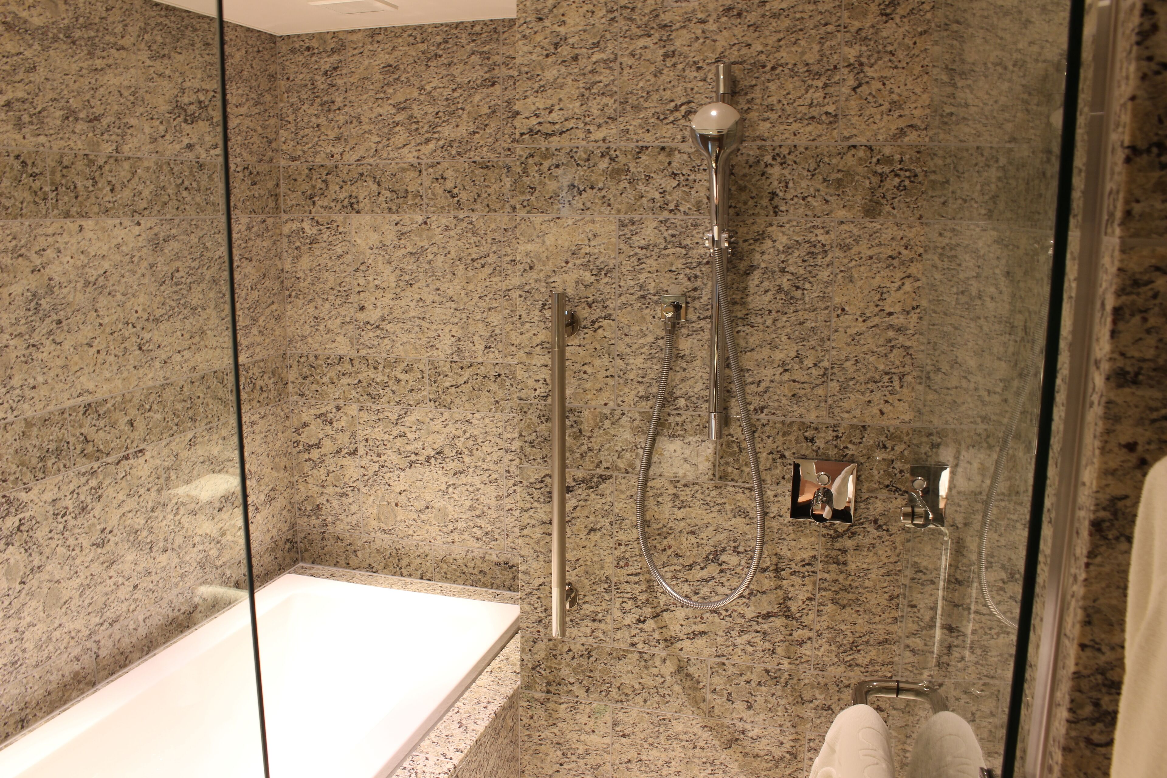A modern bathroom with a glass-enclosed shower, a standalone bathtub, and granite walls.