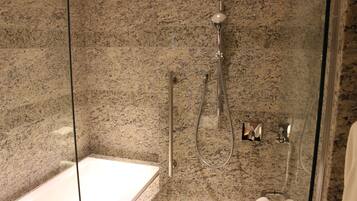 A modern bathroom with a glass-enclosed shower, a standalone bathtub, and granite walls.