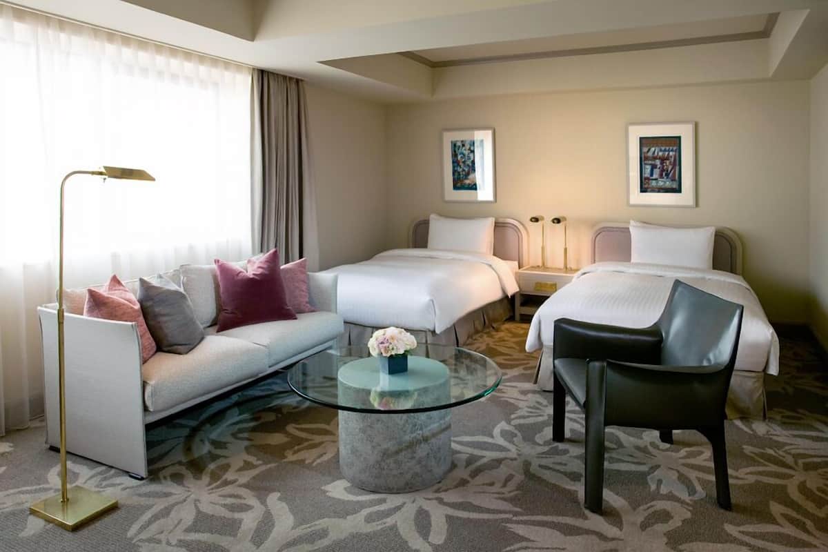 Une chambre d’hôtel avec un canapé, deux lits, une table basse en verre et une chaise.