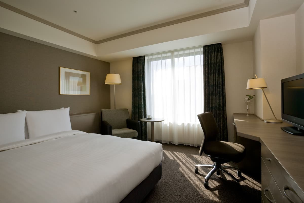Une chambre d’hôtel avec un grand lit, un bureau, une chaise, une télévision et une fenêtre avec des rideaux.