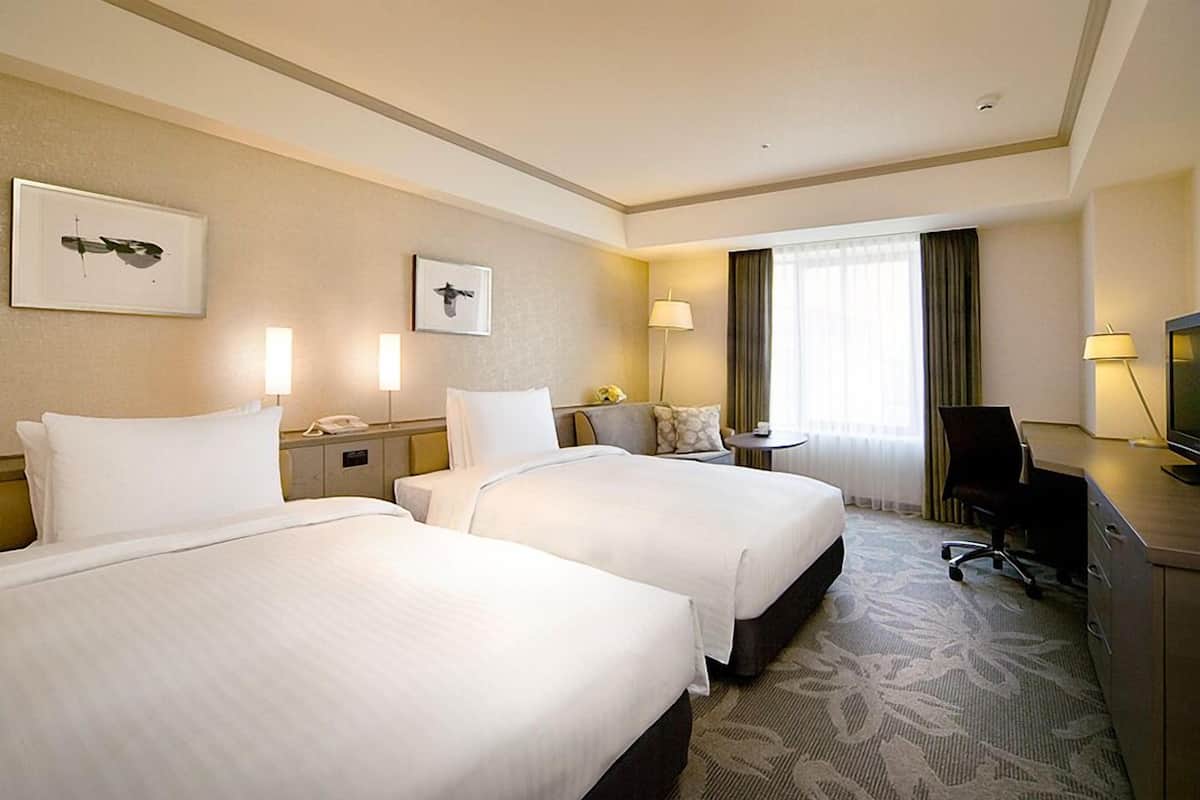 Une chambre d’hôtel avec deux lits, un bureau, une chaise, une télévision et deux lampes de chevet.