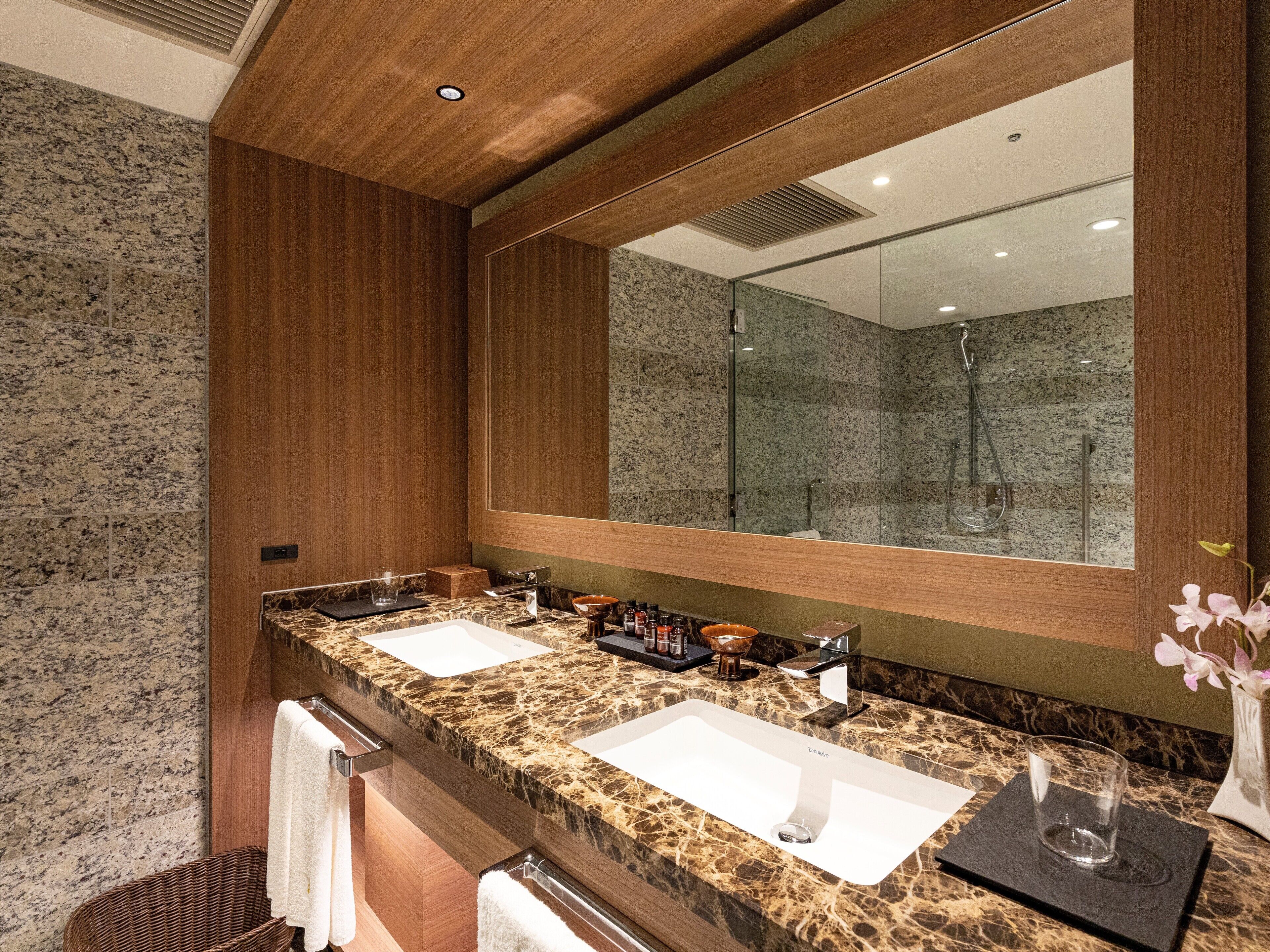 A modern bathroom with two sinks, a large mirror, and a shower.