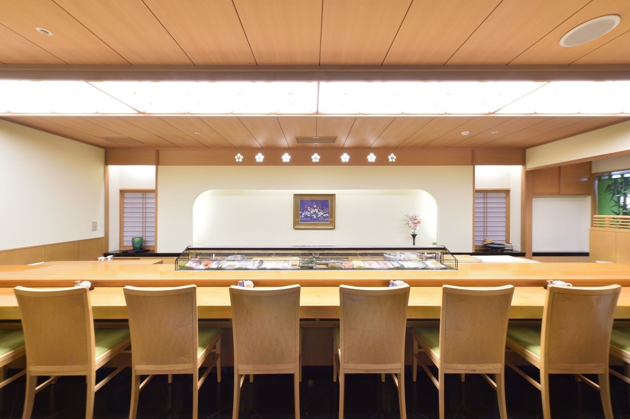 A restaurant with a long counter, wooden chairs, and a decorative wall with a framed picture.