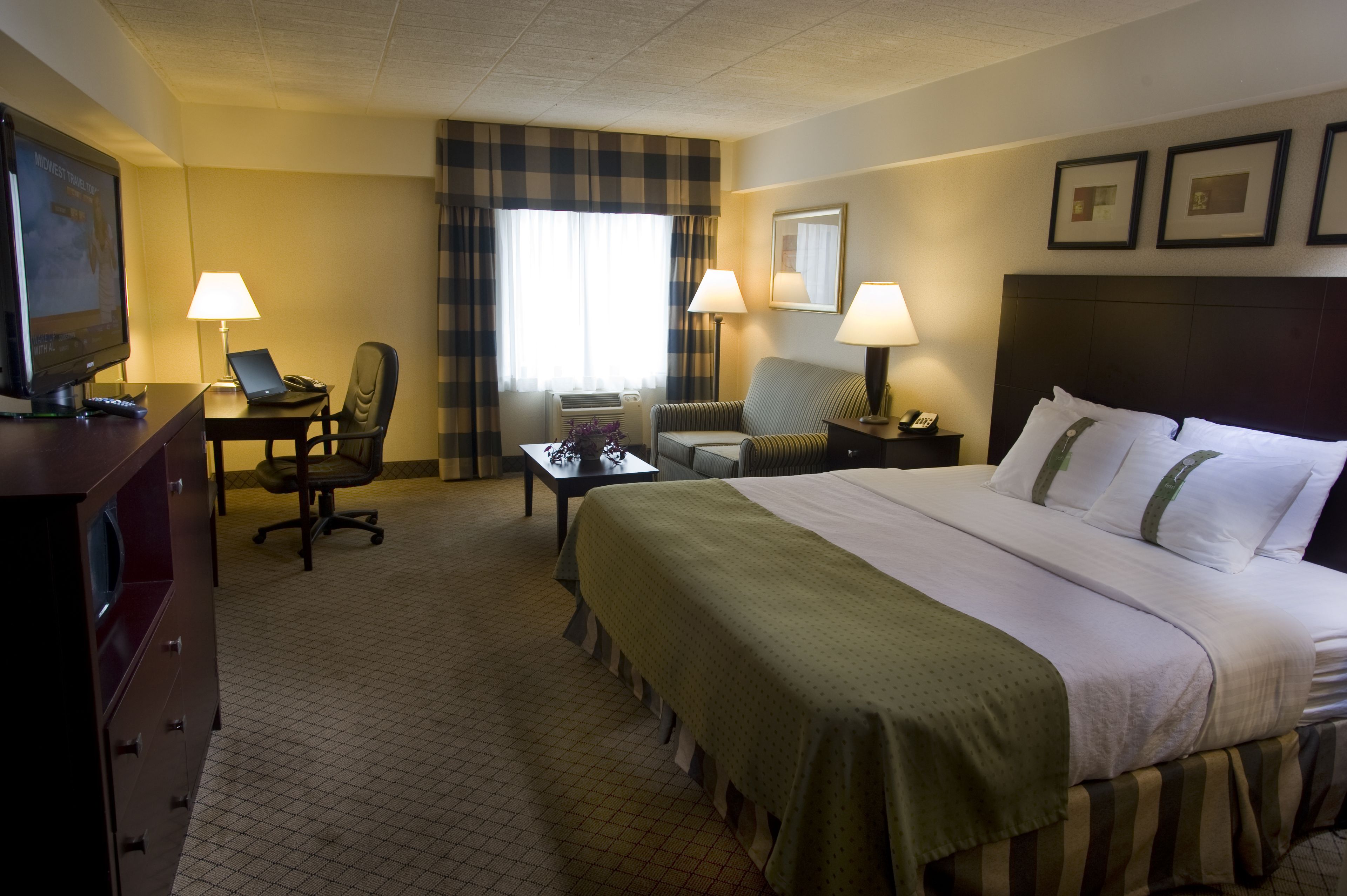 A hotel room with a bed, desk, chair, and a television.
