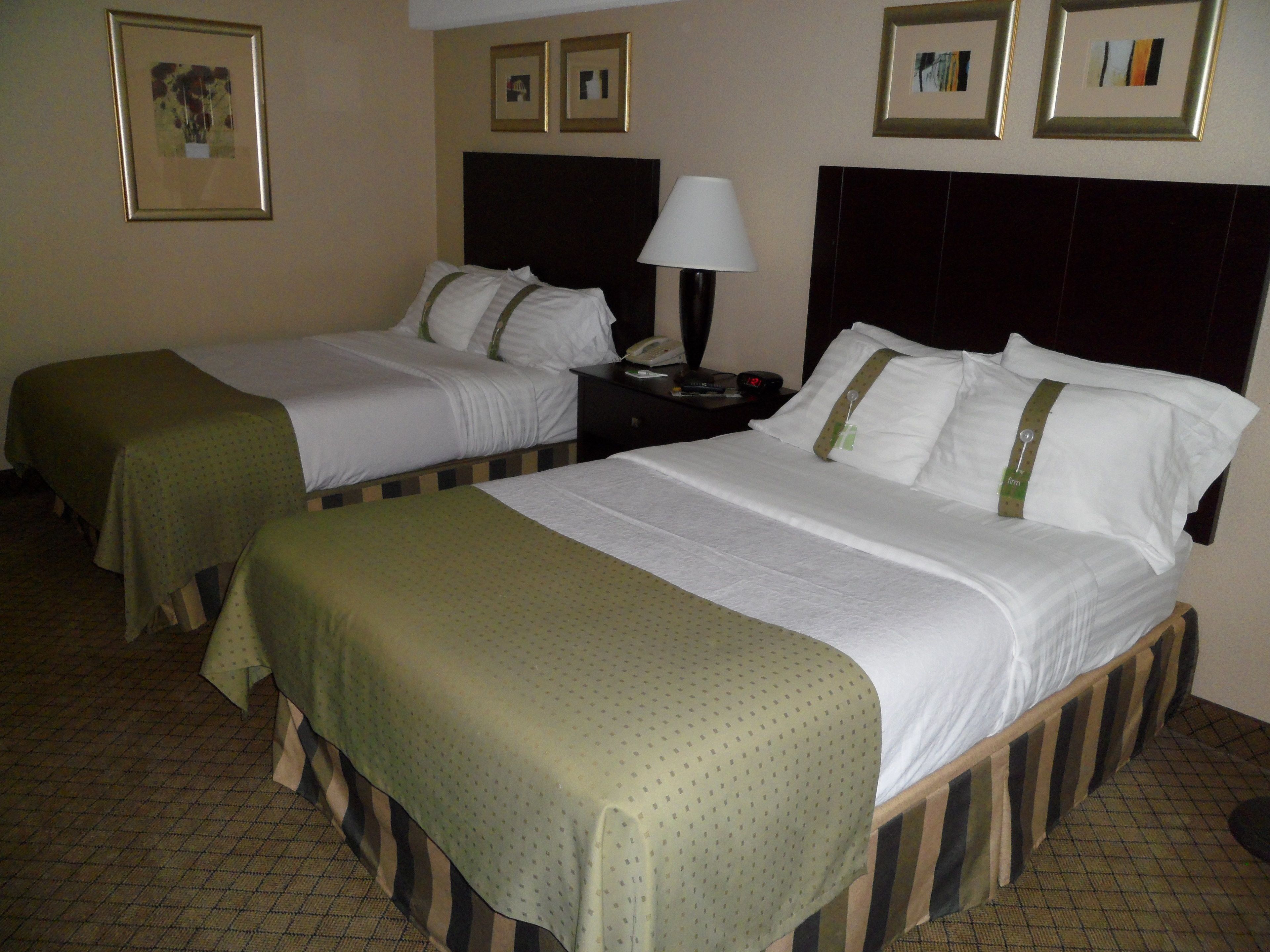 A hotel room with two single beds, a nightstand with a lamp, and framed pictures on the wall.