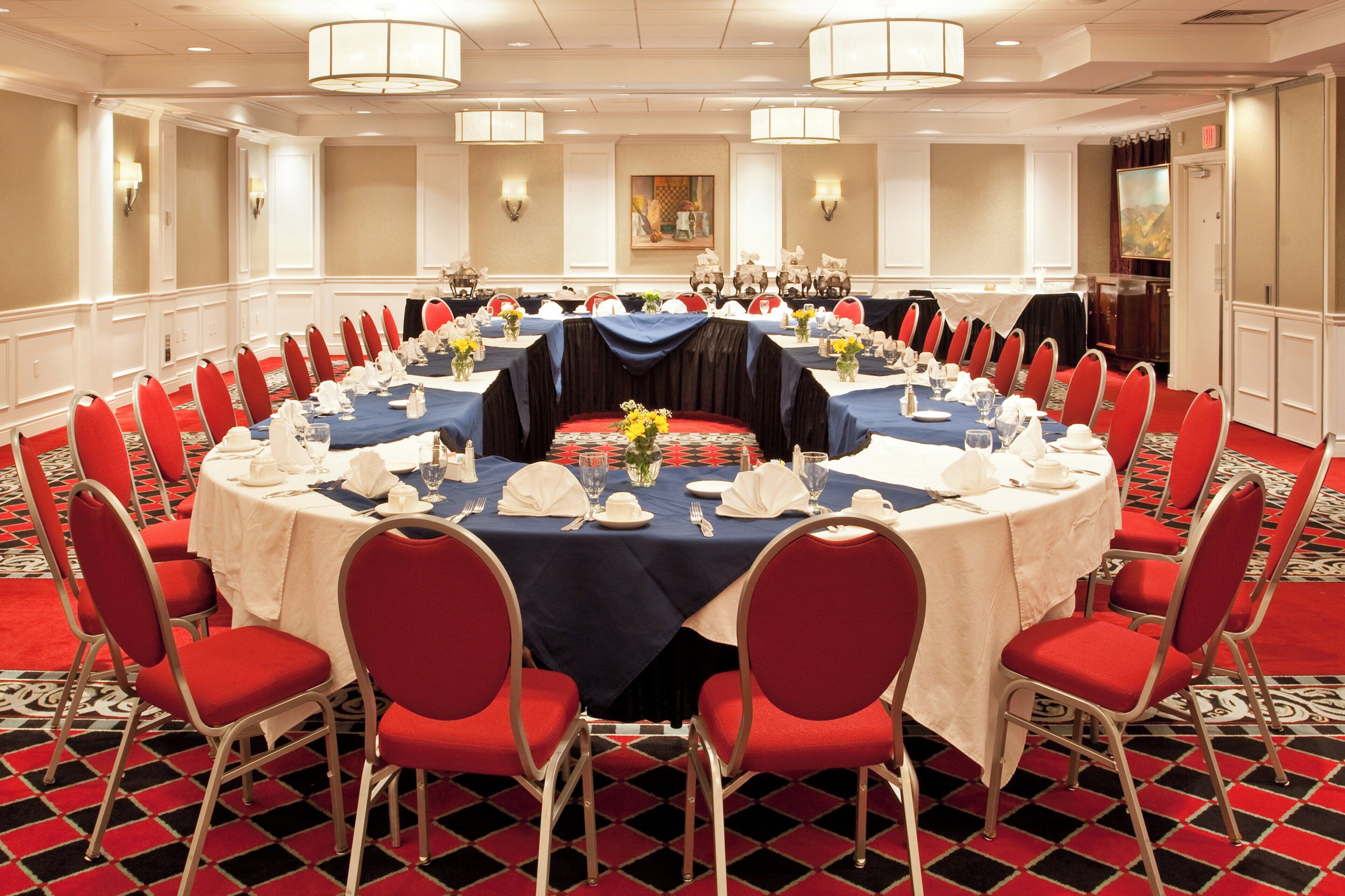 A conference room with round tables, red chairs, and a patterned carpet.