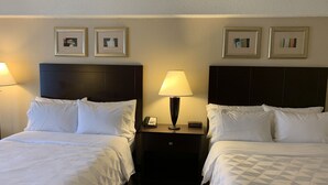 Una habitación de hotel con dos camas, una mesita de noche con lámpara y cuadros en la pared.