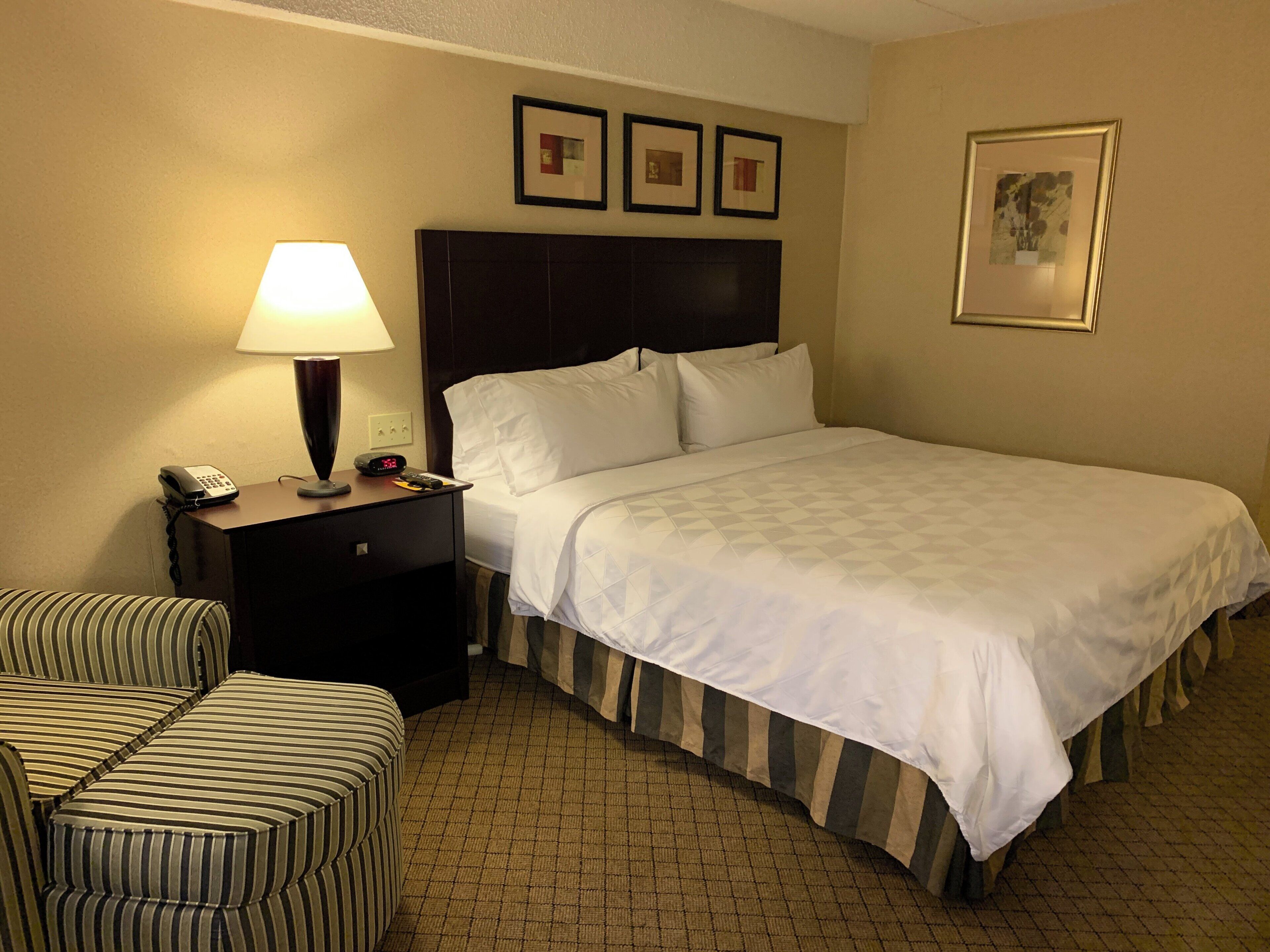 A hotel room with a bed, a nightstand with a lamp, a telephone, and a chair.