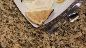 Un plato de desayuno con tocino, huevos, tostadas y gajos de naranja sobre una encimera de granito.