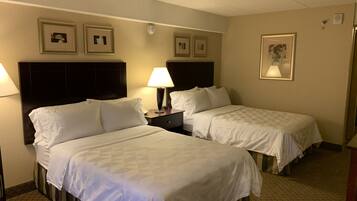 A hotel room with two beds, a nightstand, a lamp, and framed pictures on the wall.
