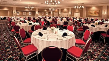 A banquet hall with round tables, red chairs, chandeliers, and a carpeted floor.