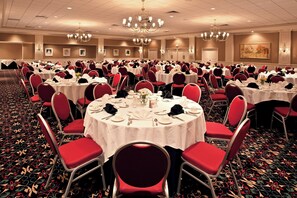A banquet hall with round tables, red chairs, chandeliers, and a carpeted floor. - Holiday Inn Johnstown Downtown by IHG (Johnstown)