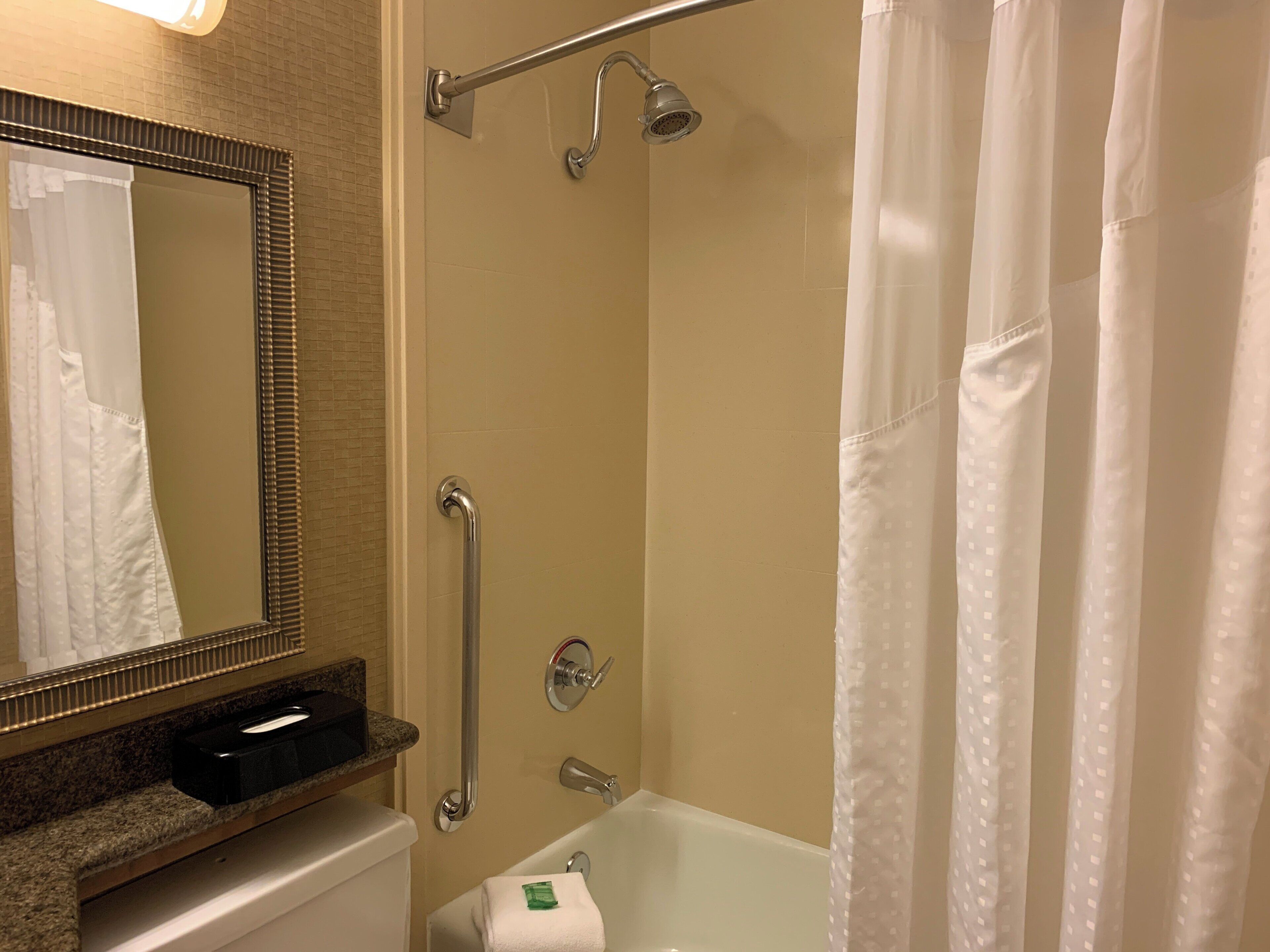 Un baño con ducha, inodoro, lavamanos con dispensador de toallas y espejo.