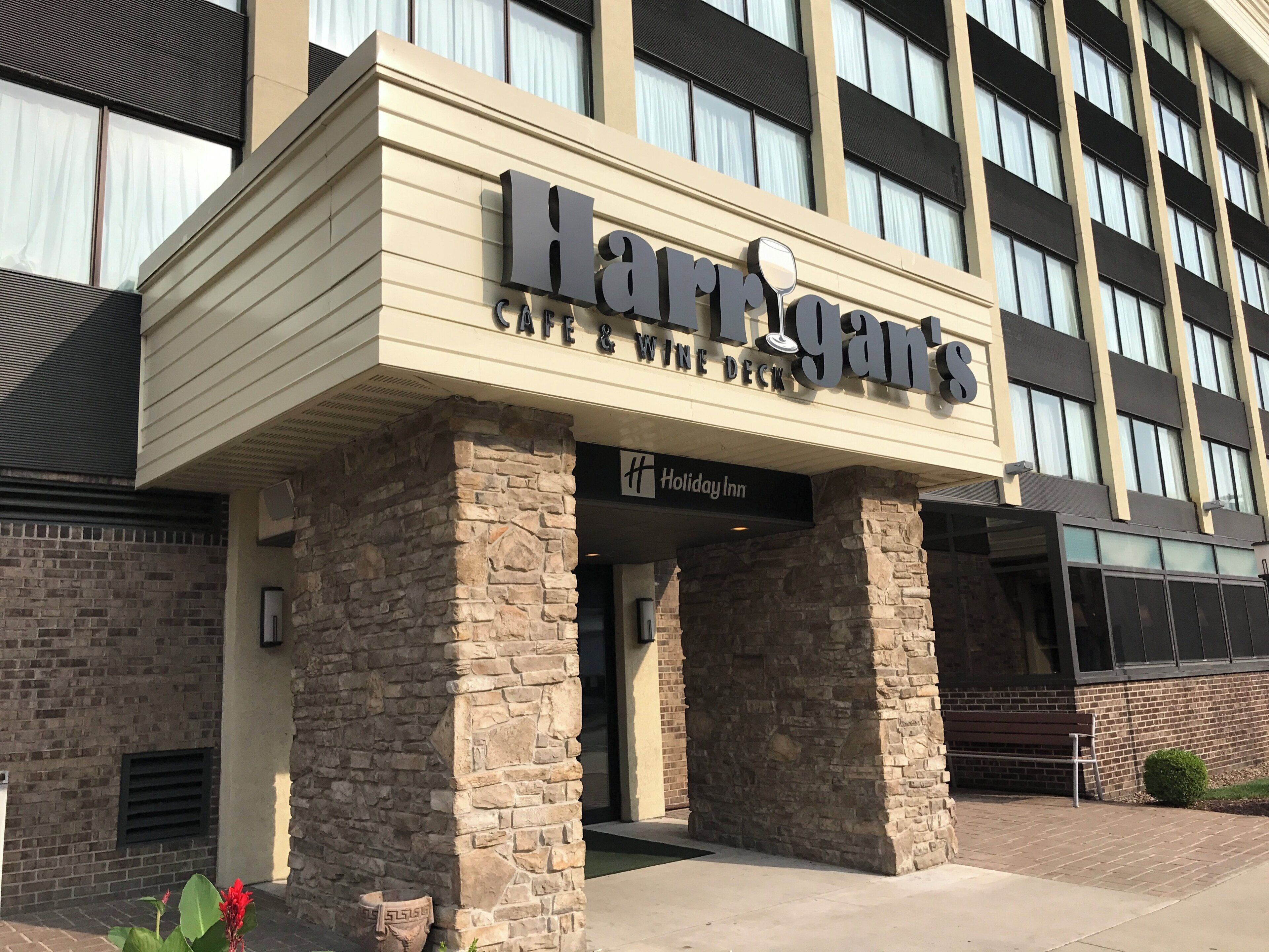 A hotel entrance with a stone facade, a sign for 'Harigans' Cafe & Wine Deck, and a Holiday Inn sign.