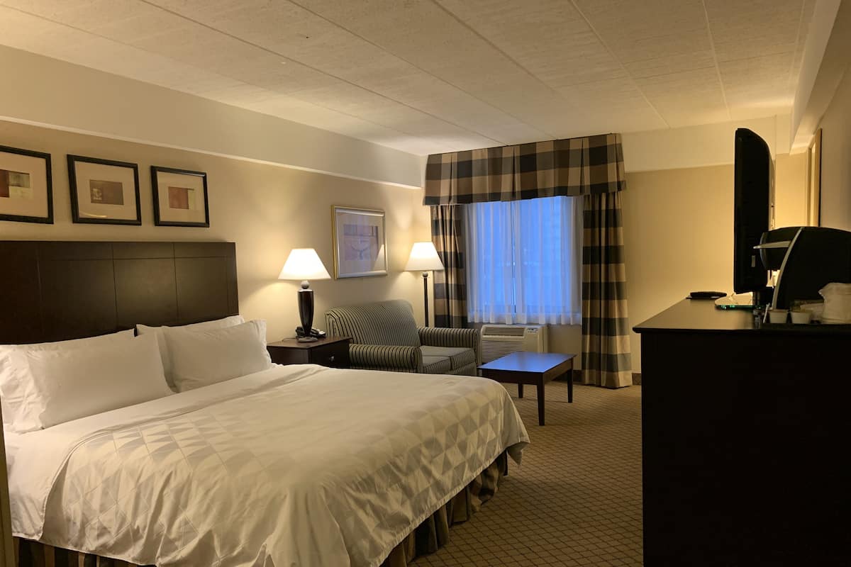 A hotel room with a large bed, a desk, a chair, a lamp, and a window with curtains.
