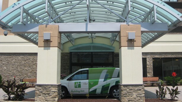Entrada de un hotel Holiday Inn con un paseo techado y servicio de transporte verde y blanco.