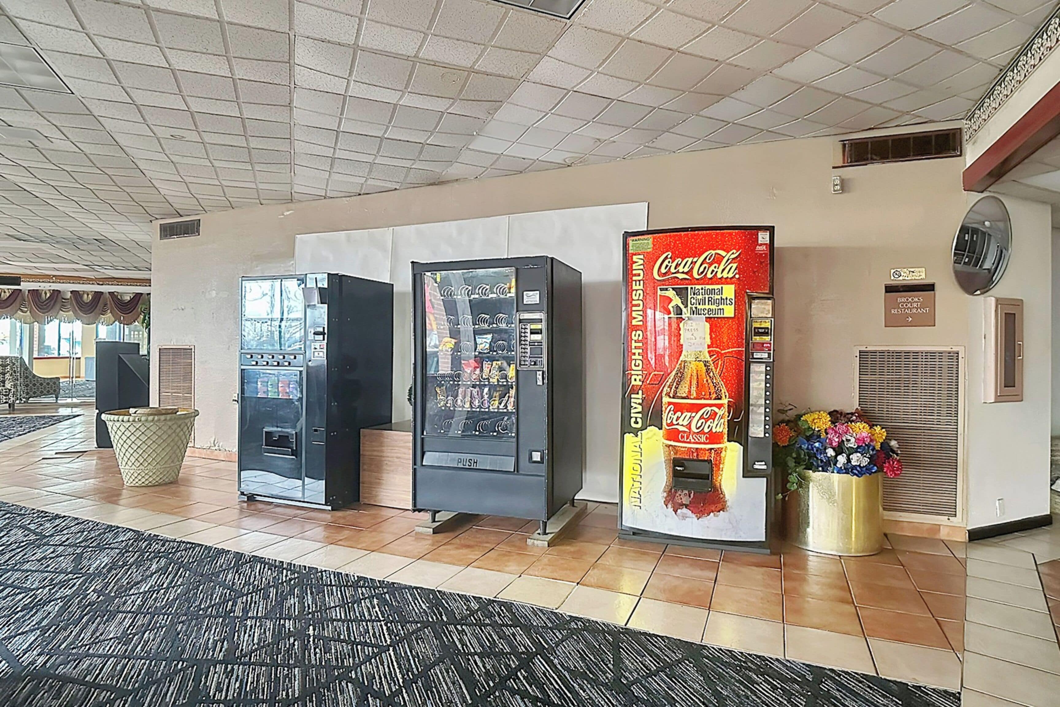 A lobby with vending machines, a Coca-Cola Classic machine, and a flower vase.