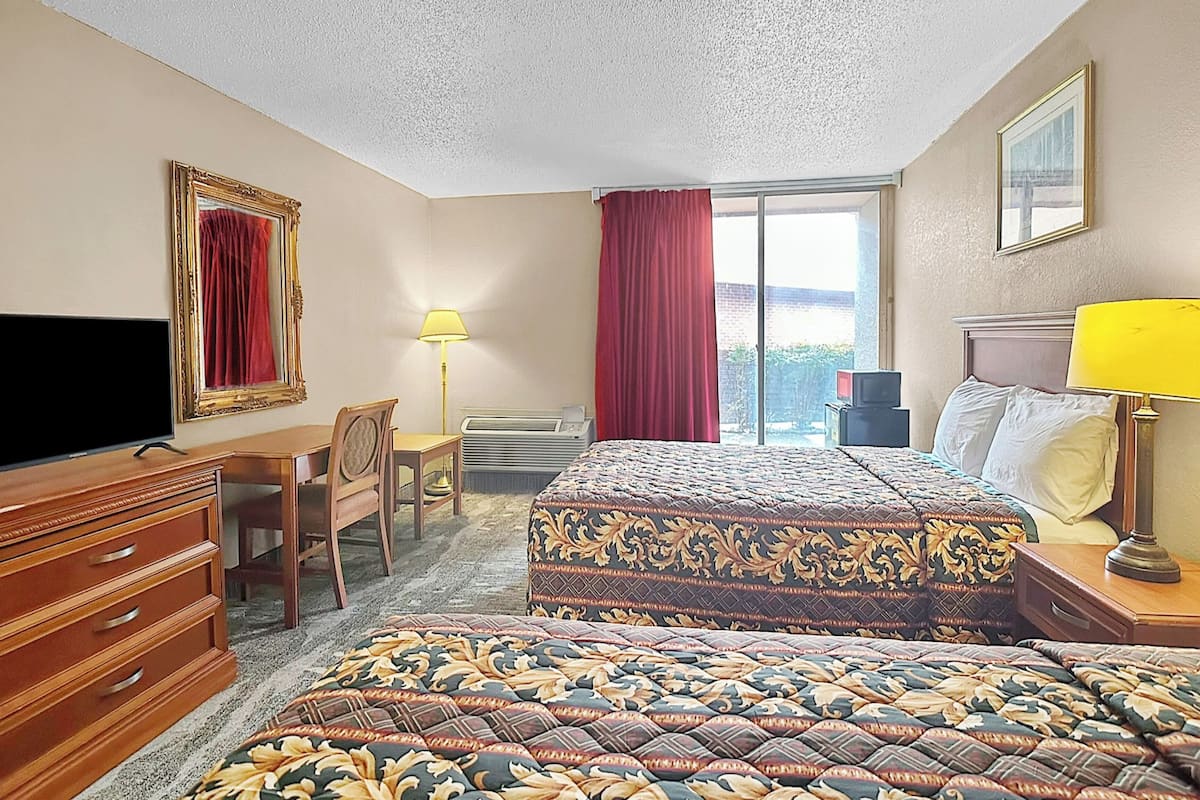 A hotel room with a bed, a desk, a chair, a television, a lamp, and a window with curtains.