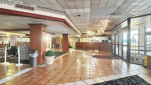 Un hall d’hôtel avec un comptoir d’accueil, une poubelle, une plante en pot et un lustre.