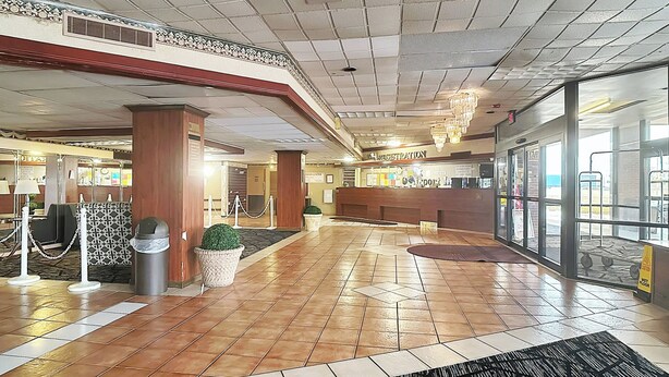Un vestíbulo de hotel con un mostrador de recepción, un cubo de basura, una planta en maceta y un candelabro.