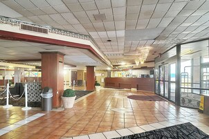 Un vestíbulo de hotel con un mostrador de recepción, un cubo de basura, una planta en maceta y un candelabro.