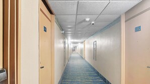 Pasillo de hotel con pisos alfombrados, puertas a ambos lados y un techo con cámara de seguridad.