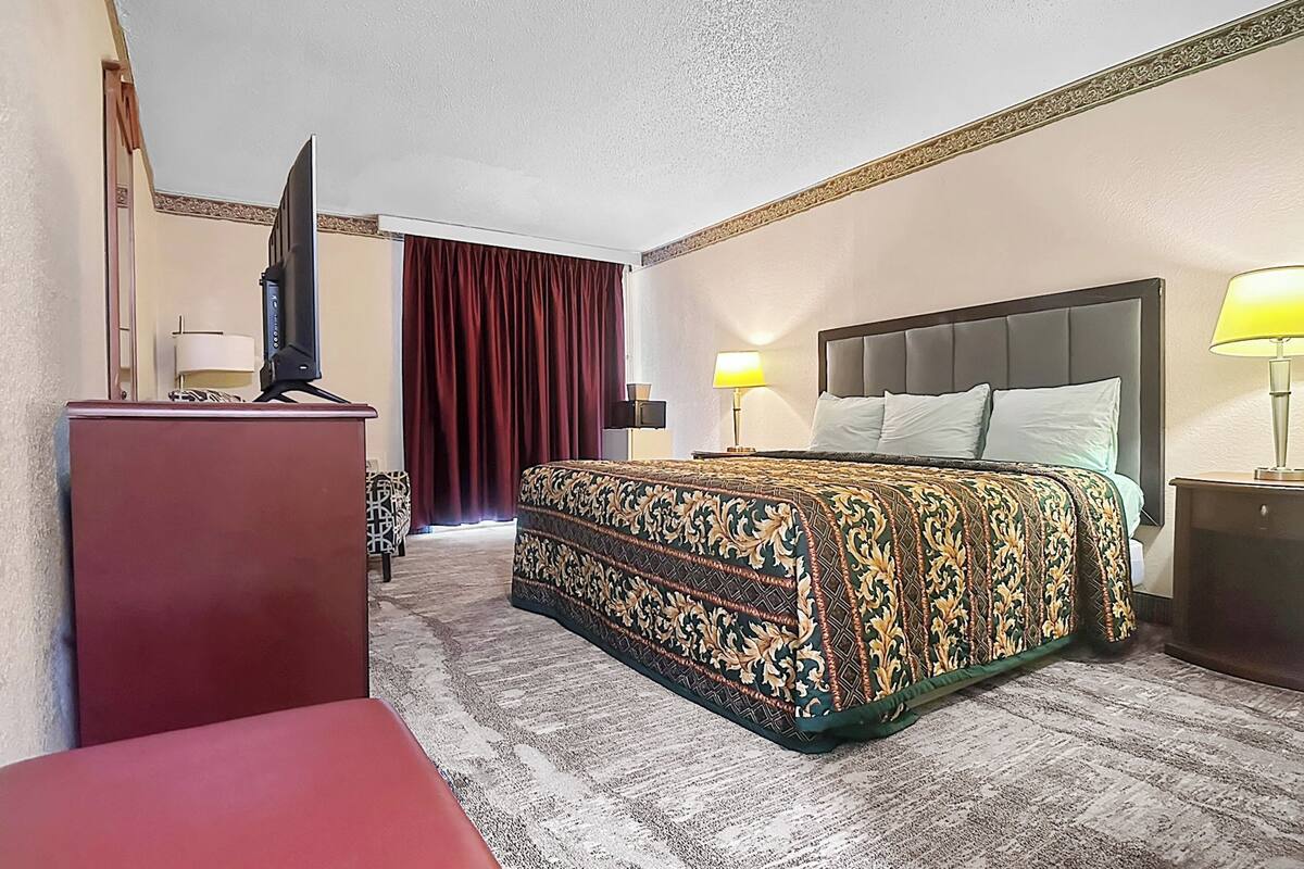 A hotel room with a bed, a desk, a TV, and two lamps.