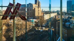 A cityscape through a window with a large building logo, various buildings, and a clear sky. - London Marriott Hotel Kensington (London)