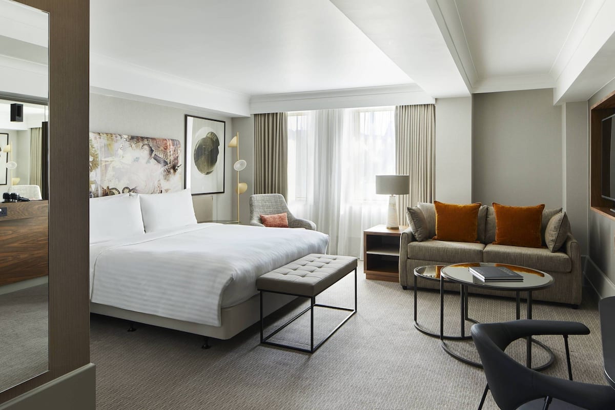A hotel room with a large bed, a sofa, a coffee table, and a chair.