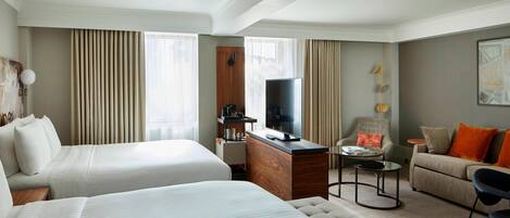 A hotel room with two beds, a desk, a television, a sofa, and a chair.