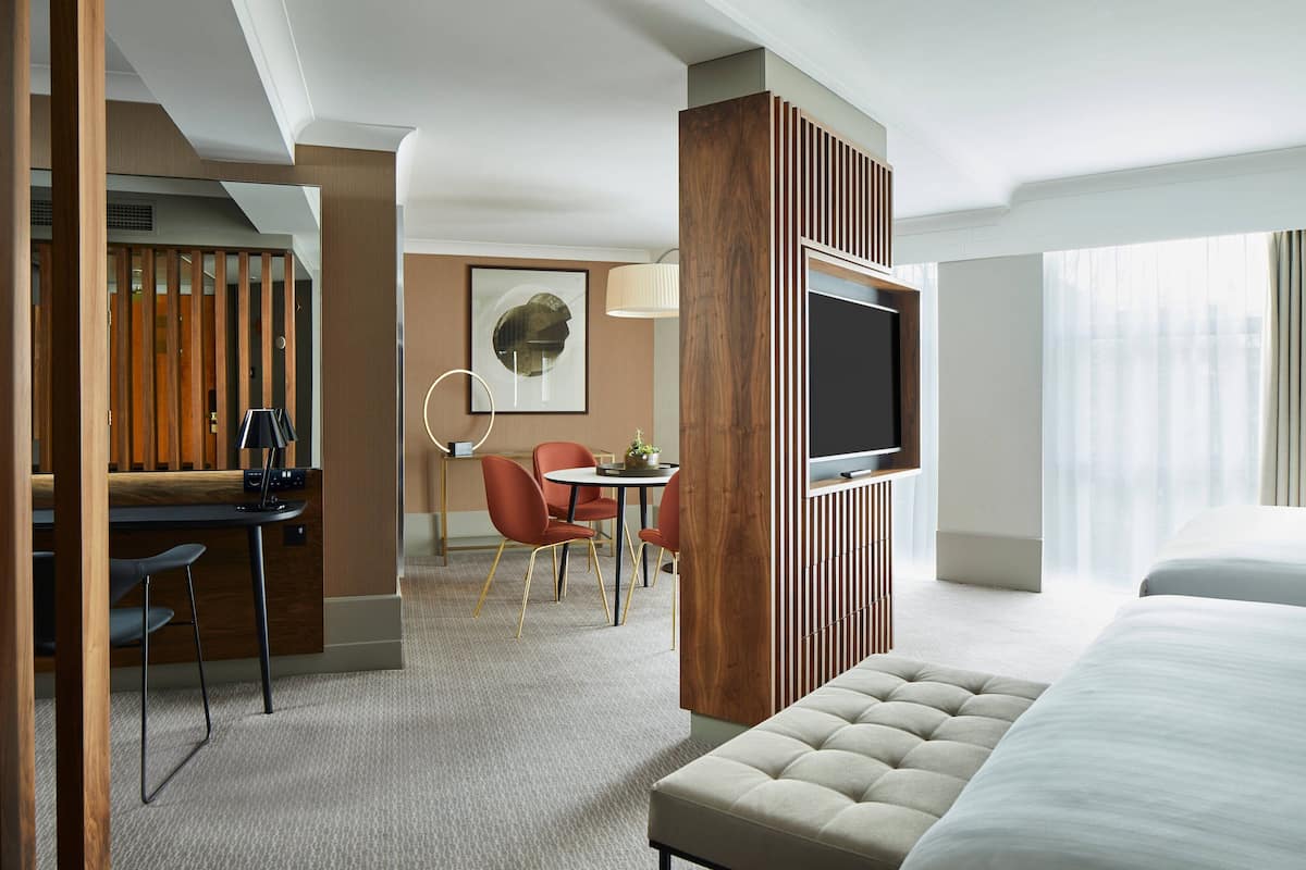 A hotel room with a bed, a desk with a chair, a TV mounted on the wall, and a window with curtains.