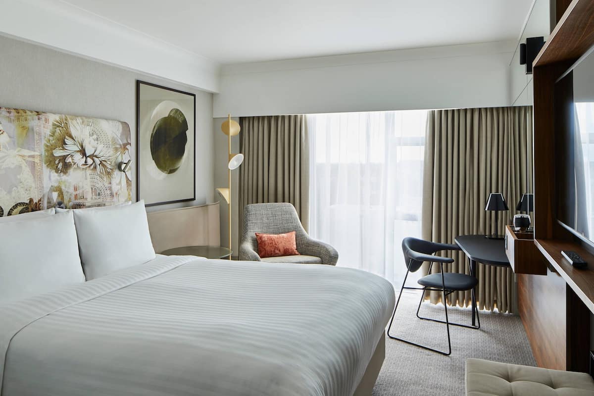 A hotel room with a large bed, a desk with a chair, a TV, and a window with curtains.