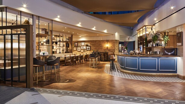 A modern interior with a bar area, seating, and a brick wall. - London Marriott Hotel Kensington (London)