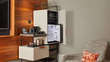 A modern room with a built-in minibar, a coffee machine, and a comfortable armchair with a cushion.
