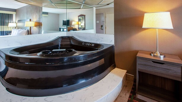 Een moderne badkamer met een zwart whirlpoolbad, een marmeren aanrechtblad en een houten nachtkastje met een lamp.