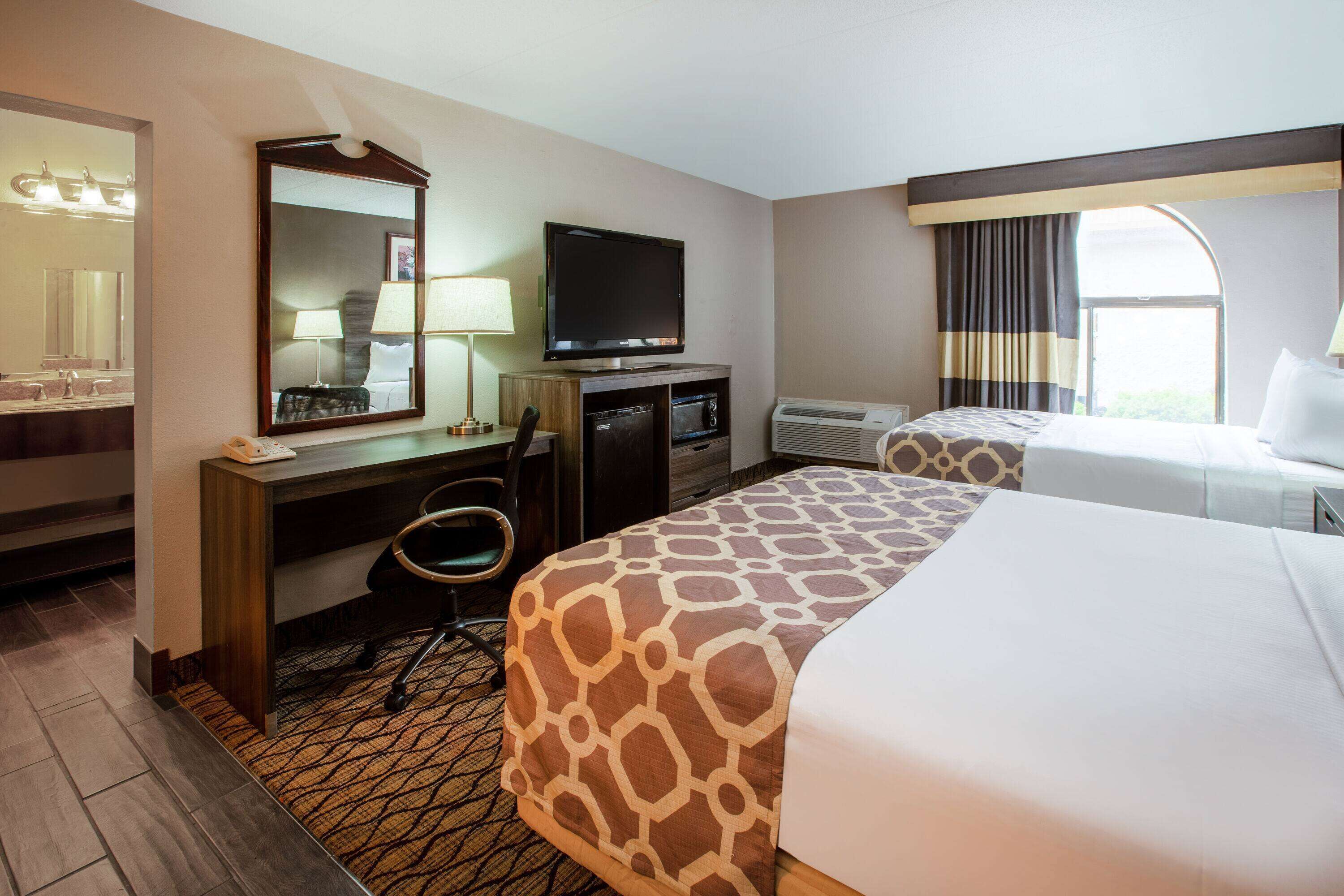 A hotel room with a large bed, a desk with a television, a chair, and a window with curtains.