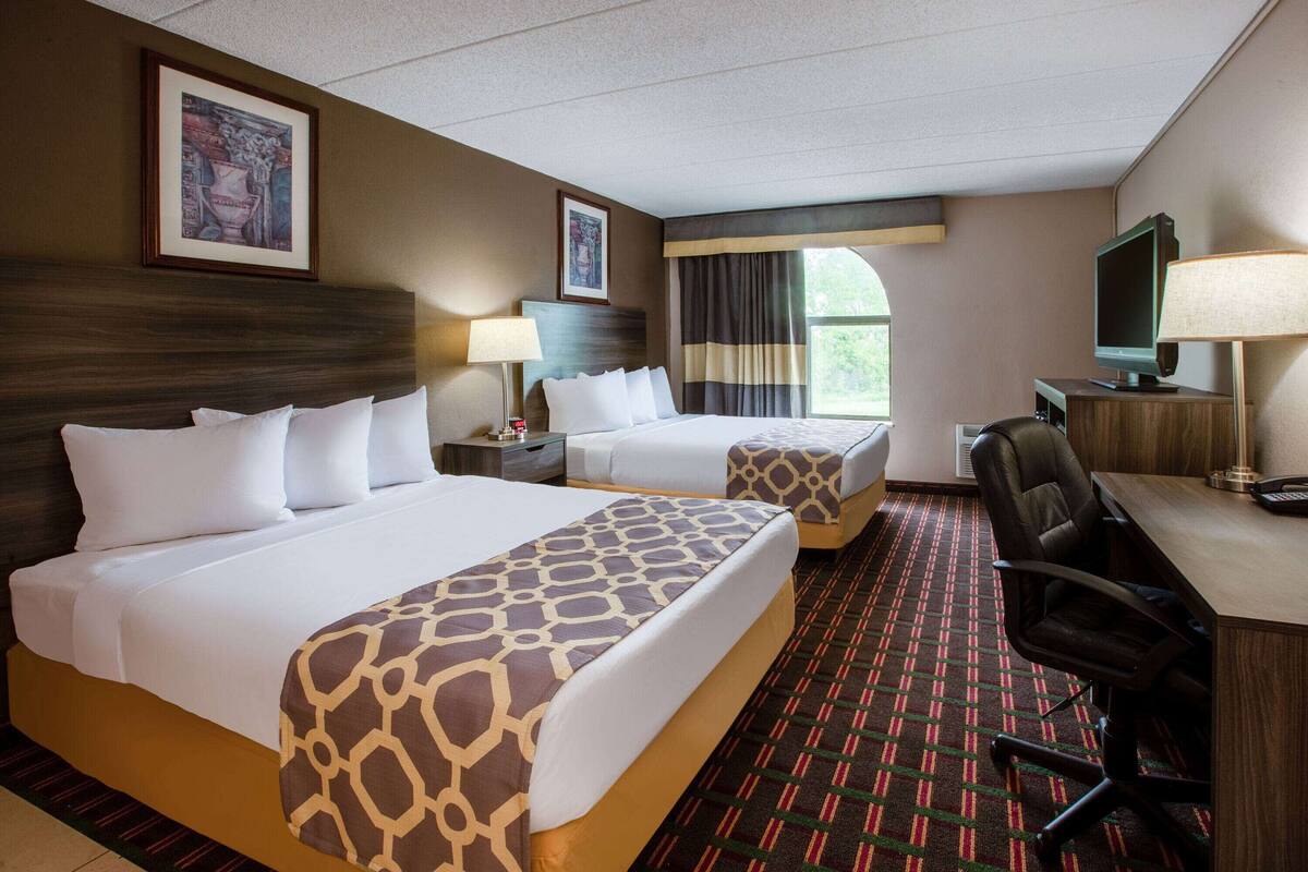 Une chambre d’hôtel avec deux lits, un bureau, une chaise, une télévision et des œuvres d’art accrochées aux murs.