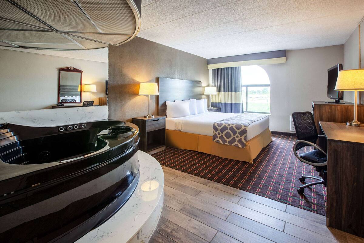 Une chambre d’hôtel comprenant un lit, un bureau, une chaise, une télévision, une lampe, un miroir et une baignoire.