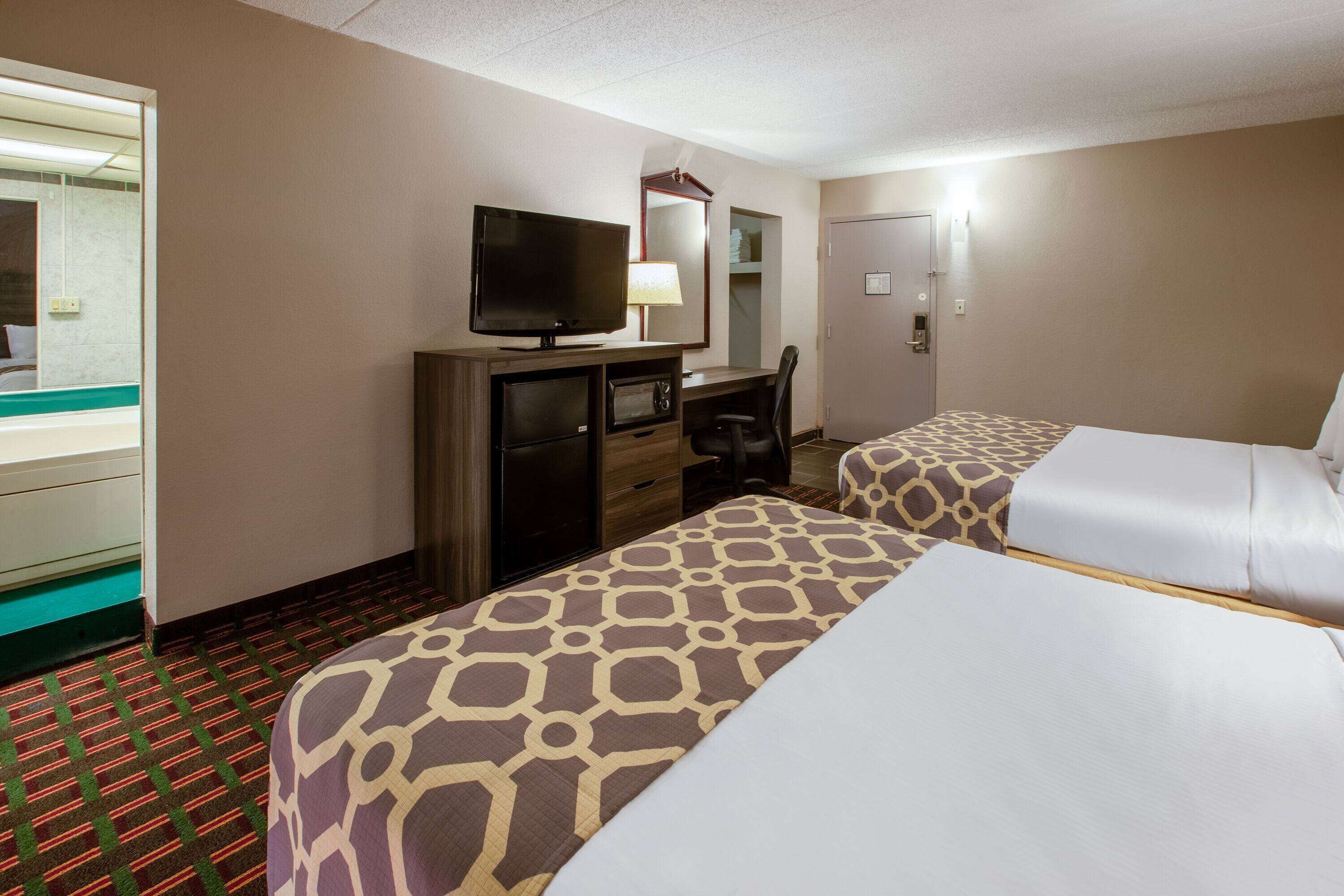 A hotel room with two beds, a desk with a television, a mirror, and a wardrobe.