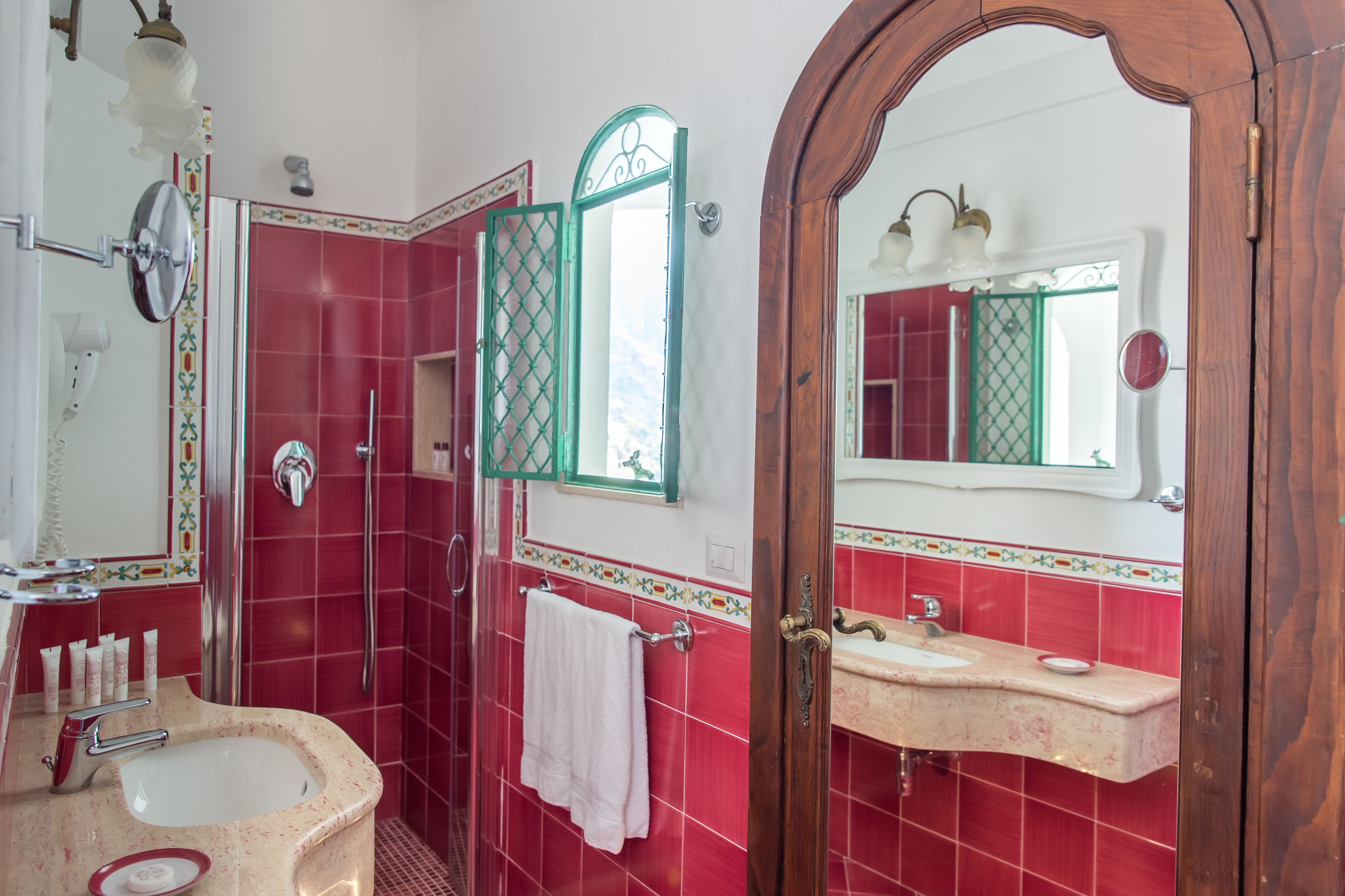 A bathroom with a red tiled wall, a white sink, a mirror, and a shower area.
