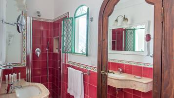 A bathroom with a red tiled wall, a white sink, a mirror, and a shower area.