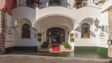 Entrada de hotel con alfombra roja, arcos y plantas en macetas.