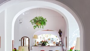 Una habitación con un arco blanco, una planta colgante, un espejo, una mesa con sillas y una ventana con vistas.