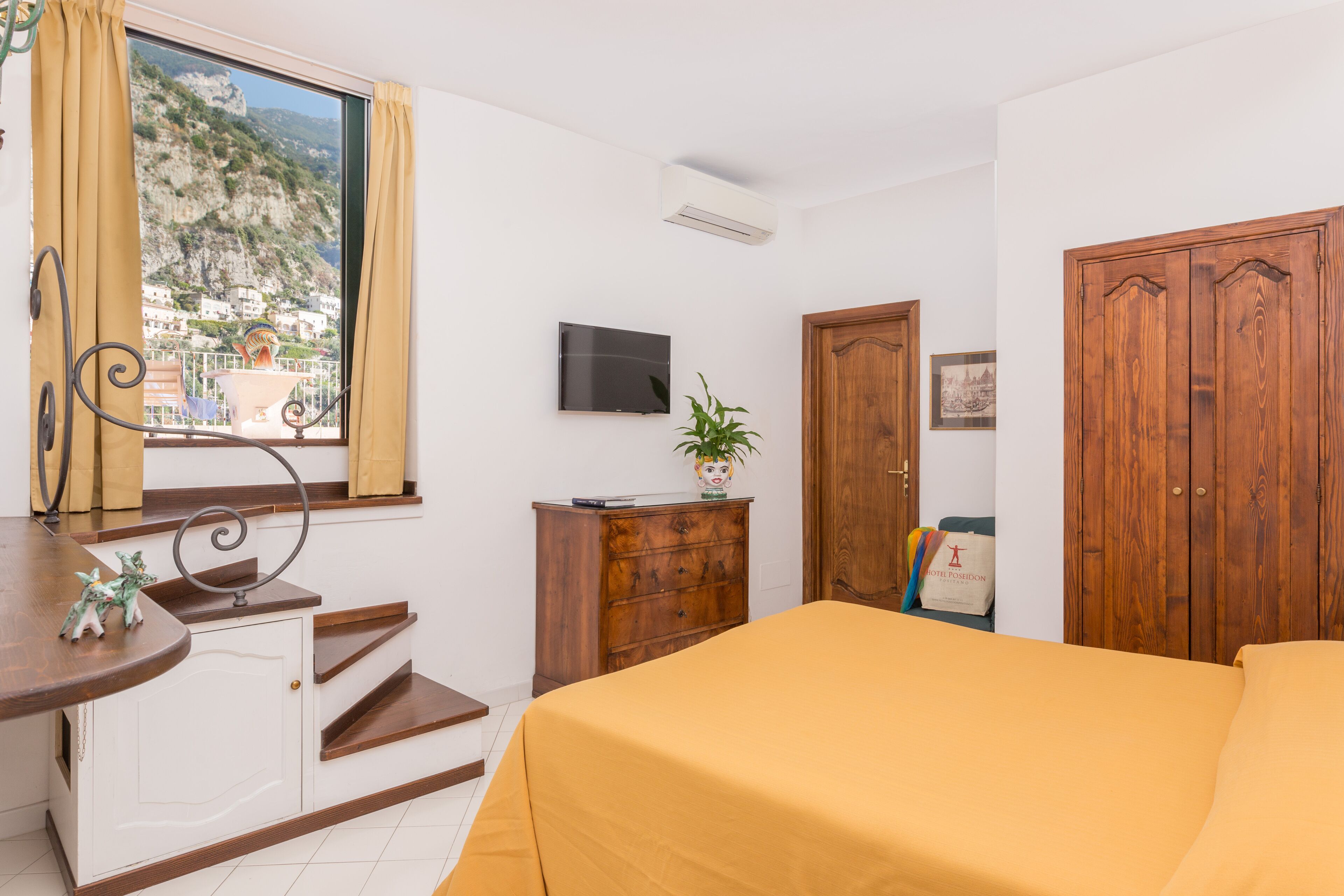 Quarto com cama, escrivaninha, televisão, guarda-roupa de madeira e janela com cortinas.