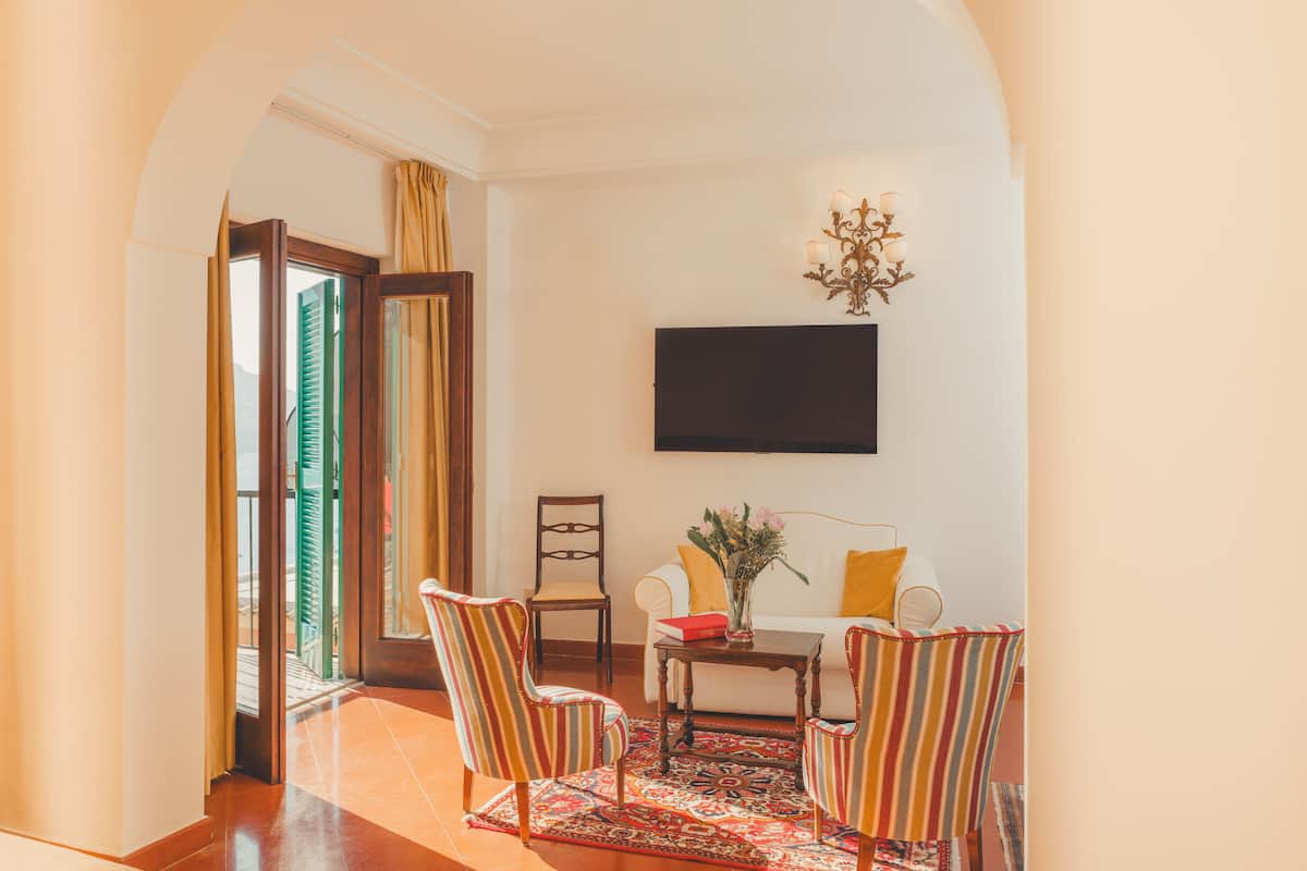 Una habitación con un sofá, dos sillones a rayas, una mesita de centro, un televisor de pantalla plana y una araña.