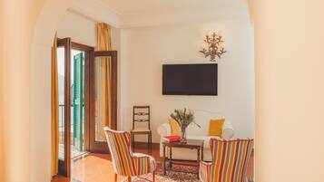 A room with a sofa, two striped armchairs, a coffee table, a flat-screen TV, and a chandelier.