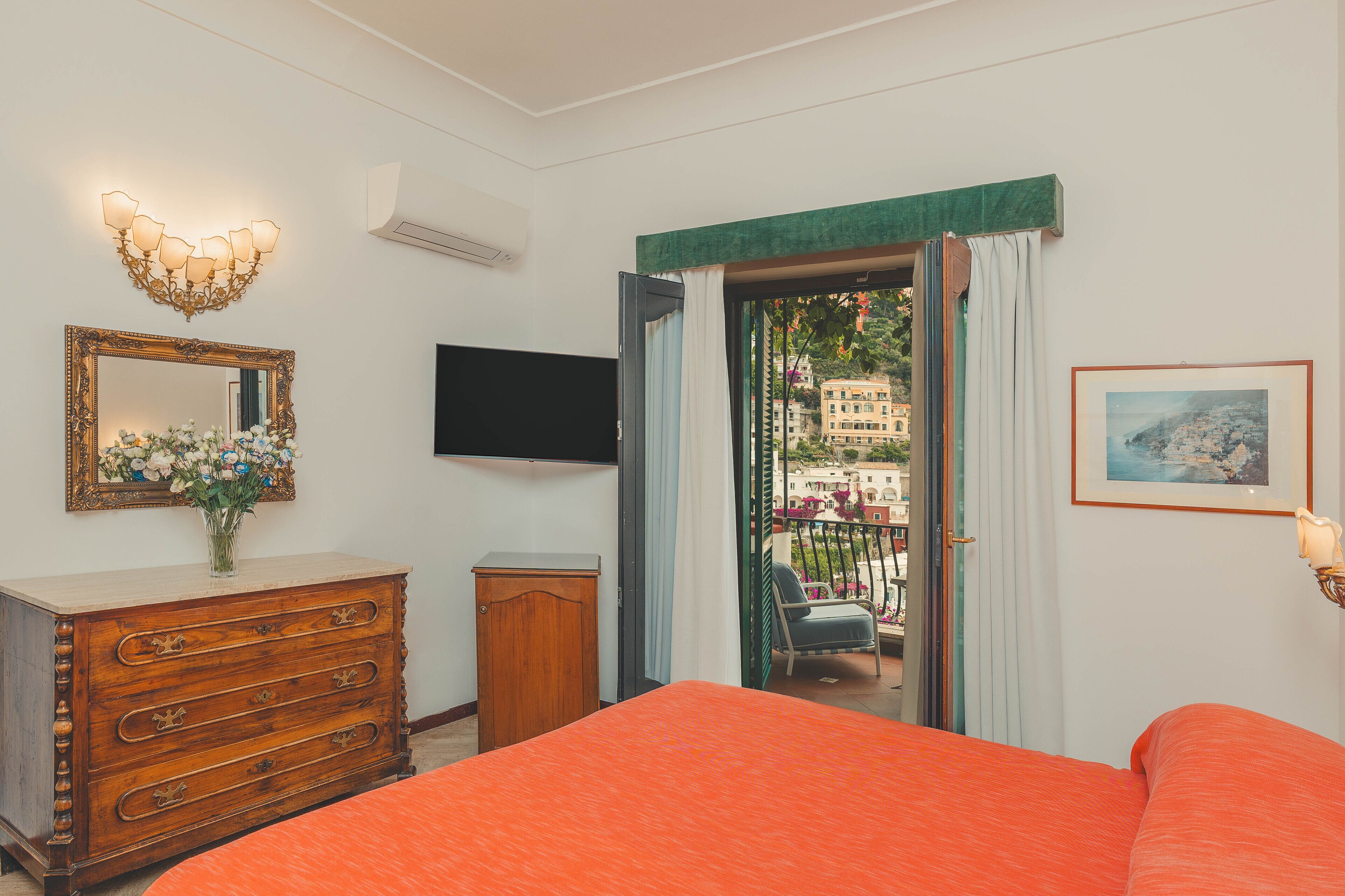 Una camera da letto con un letto grande, una cassettiera, una TV, uno specchio e un balcone con vista sugli edifici.