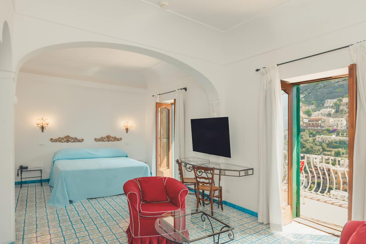 Una habitación de hotel con cama, televisión, mesa de comedor con sillas y balcón con vistas.