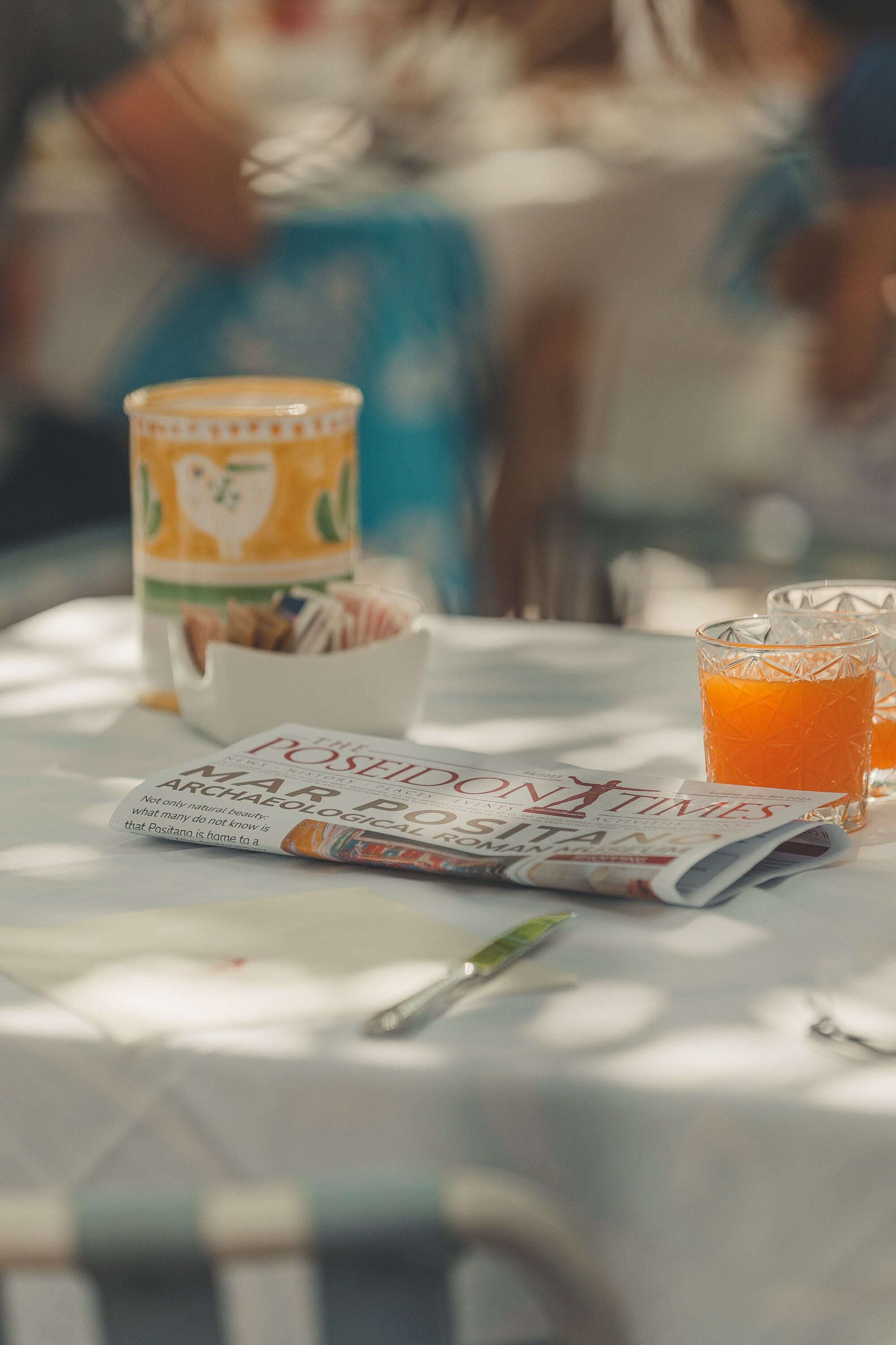 A table with a newspaper, a glass of orange juice, and a container of snacks.